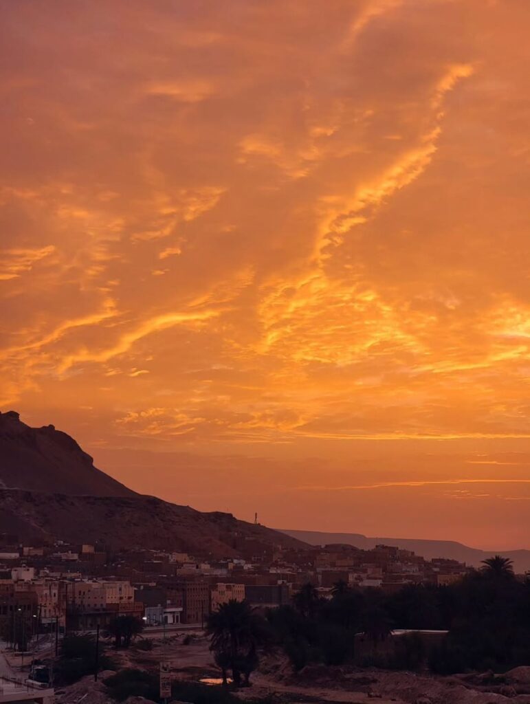 Beautiful sunset over Tarim City buildings and palm trees with mountains in the background.