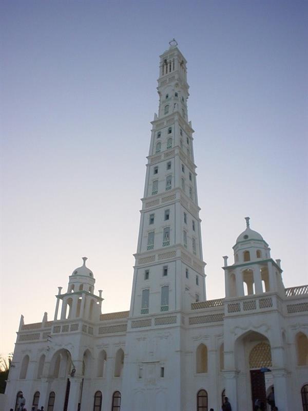  A striking upward-angle shot of the iconic Al-Mihdhar Mosque in Tarim, highlighting its remarkably tall, intricately decorated mud-brick minaret against a deep blue sky.