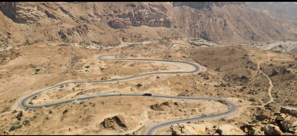 A winding mountain road cutting through a desert canyon landscape in Yemen.